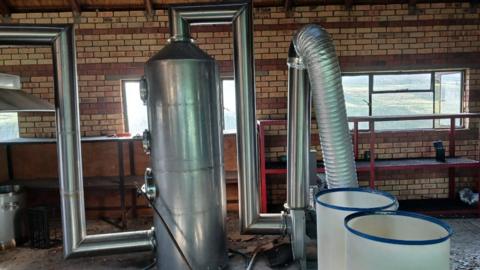 Industrial-sized metal laboratory equipment. Pipes can be seen connected to a distillation unit.