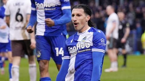 Yusuf Akhamrich slides on his knees with his hands by his side after scoring a goal