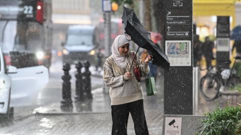 A woman tries to reverse her inside out umbrella in rainy conditions 