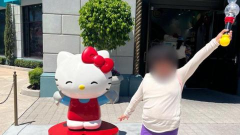A girl wearing a white top and purple trousers holds a toy aloft in front of a cartoon character in Disney World in Florida.