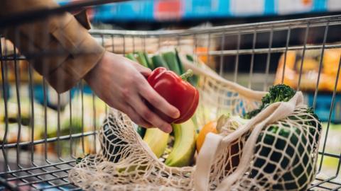 Close-up shot of a hand putting a red bell pepper into a mesh grocery bag