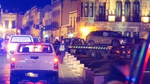 Police forces work at the scene as they remove a vehicle with bodies that were left by unknown assailants in front of the Government Palace