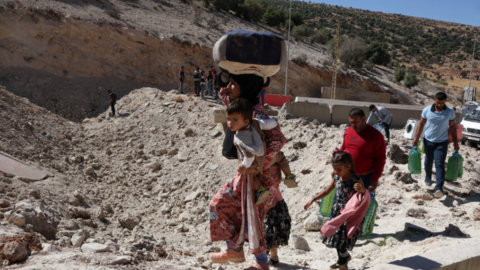 A family with two children walk on foot - the mother bearing her youngest and several bags - past the cratered road at the Masnaa crossing into Syria on 4 October