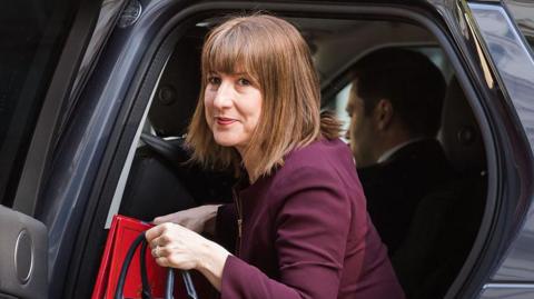 Chancellor Rachel Reeves getting out of a cab outside Downing Street in May, wearing a maroon suit and carrying a handbag and red folder