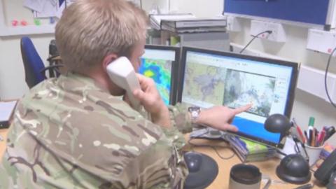 Simon King, weather presenter and RAF reservist studying weather forecast charts and briefing on the telephone.  