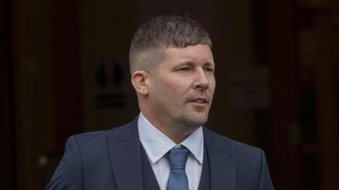 A man wearing a navy suit, blue shirt and blue tie.