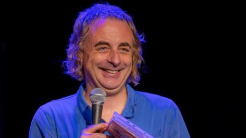 A man in a blue shirt holds a microphone