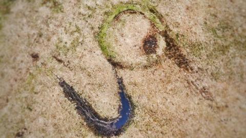 An aerial photo of the Tor Clawdd ring cairn on Mynydd y Gwair common near Swansea. Muddy tracks left by off-road bikers are clearly visible.