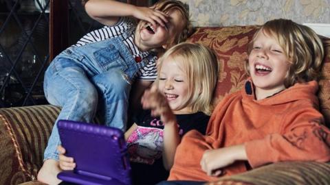 Children playing with tablet device and laughing