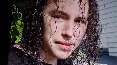 Portrait photo of Vlad Nikolin-Caisley looking to camera. He has curly long dark brown hair.