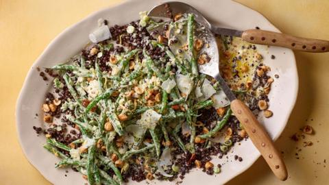 A white dish with string beans, lentils, hazlenuts, as well as two salad spoons 