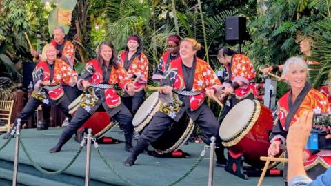 A group of women dressed in traditional Japanese clothing while playing drums.