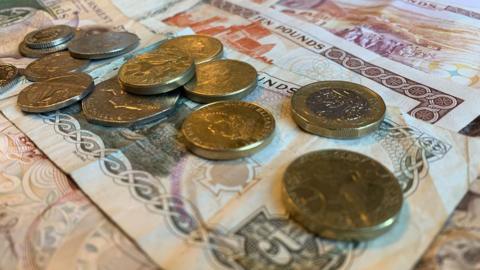 Loose change laid on top of a number of Manx £5 and £10 notes that have been spread out.