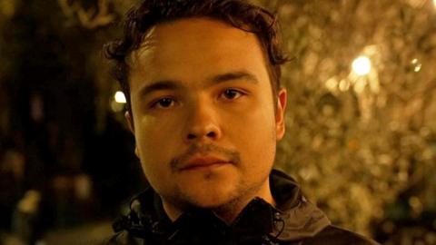 Close up headshot of Jack, taken inside lit by artificial light. He has dark hair, a moustache and beard.