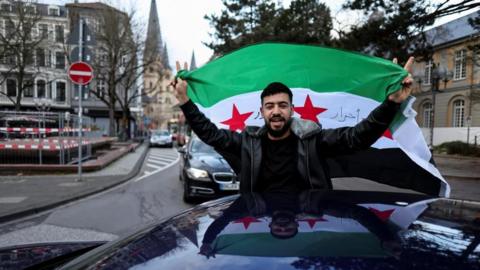 A man holds a Syrian flag in a car in Germany as he celebrates the downfall of Bashar al-Assad in his home country