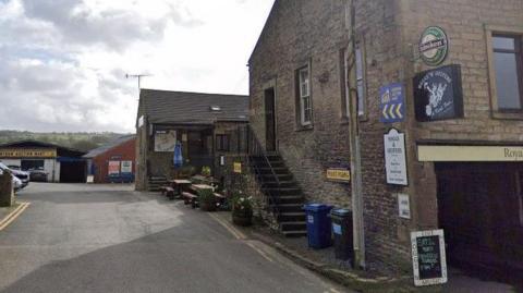 Exterior of brick pub building and car park. The outside of the pub is covered in signage advertising drinks and events. 