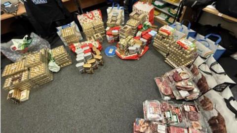 A large pile of stacked-up chocolates, meats and carrier bags all laid out on the floor in an office.