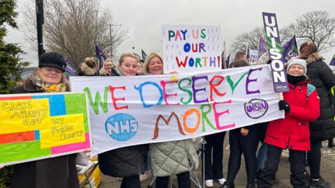 Healthcare workers standing on a picket line with signs asking for more money