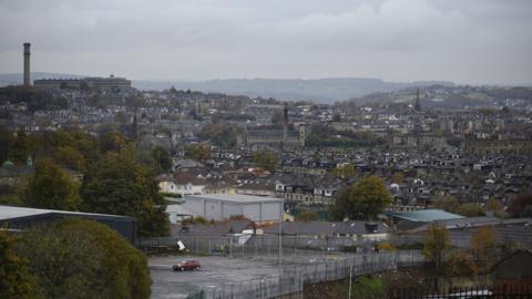 The Bradford skyline, viewed on a cloudy day. Rows of housing, trees and industrial buildings can be seen. 