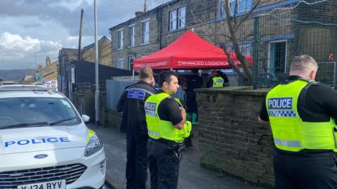 A police car and police officers positioned outside an address on a residential street.