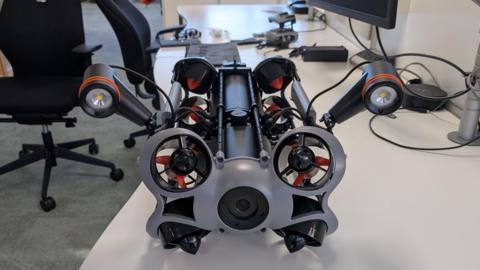 A drone sitting on a desk. There are office chairs in the background.
