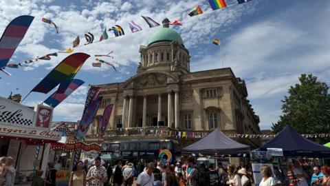 Rainbow bunting and other flags adhorn the Queen Victoria Square. Hull City Hall is centre stage. Food stalls are also set up.