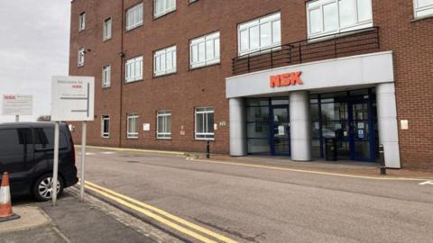 A brick building with large metal shutter in the middle. A sign at the top states NSK Newark plant.