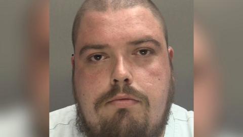 A police mugshot of Richard Britton, he has a shaved head and a beard.