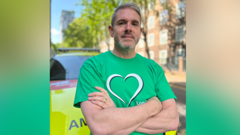 Stuart stands in front of an ambulance car with his arms crossed