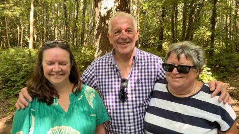 Lauren Sykes, Chris Couch and Julie Read from The Friends of Oaken Wood standing in front of a large oak tree in Oaken Wood, Barming