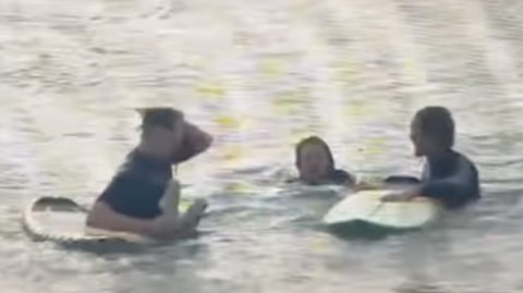 Two surfers with boards and a young woman swimming between them.