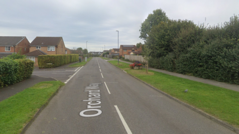 A Google Streetview of Orchard Way in Peasedown St John near Bath. A series of modern brick houses are seen on either side of the road
