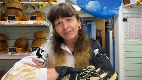 A woman stands with her arms crossed in front of bread