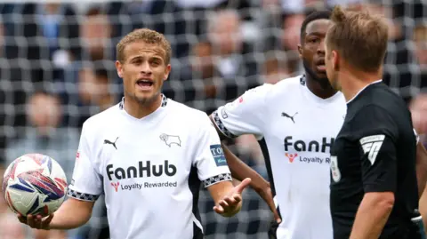 Derby County's Kenzo Goudmijn (left) and players speak to referee Oliver Langford