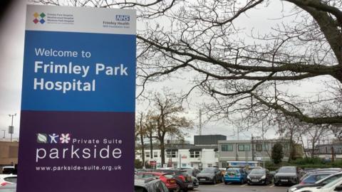 General view of hospital with car park and signage in the foreground.