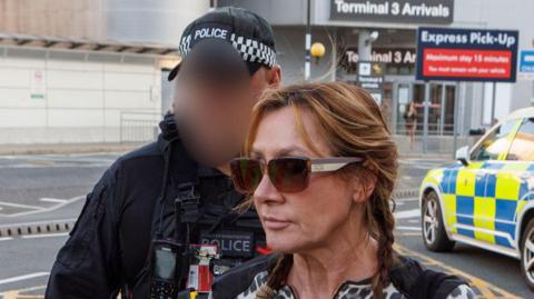 A woman in designer sunglasses and a leopoard print top is escorted into a van by police from an airport terminal.