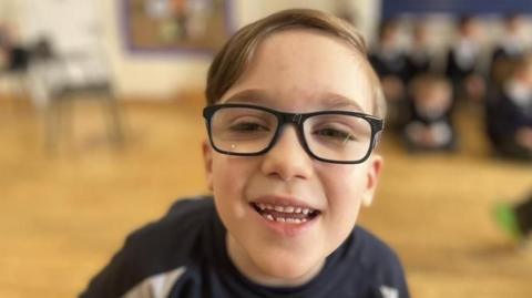 Ernie wearing glasses with black rims and navy uniform. He has light brown hair swept to one side and is smiling.