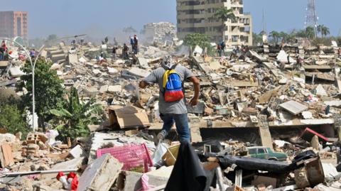 A man with a Venezuelan flag-themed backpack walks amid rubble of collapsed buildings after earthquakes hit the country, in La Guaira, Venezuela