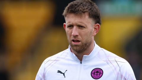 Will Aimson wearing a white Wigan top with purple Wigan badge looks forward