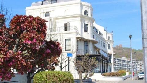 A large while building, Victorian style, sits on Dover seafront. There are trees in the photo.