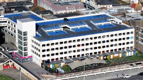 Aerial image of a multi-storey car park. It is a large white building but with dirty marks across the front of the building.