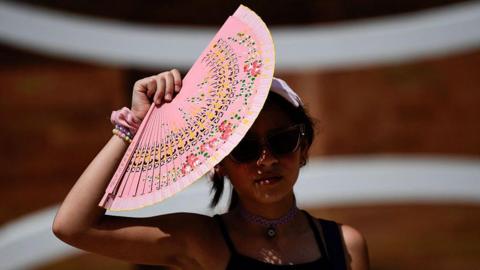 A woman shields herself from the sun with a fan