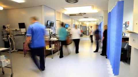 Hospital staff are blurred are they walk around a hospital ward. 