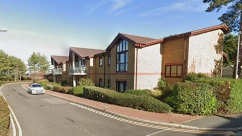 A block of flats with a car on a road in front of it.
