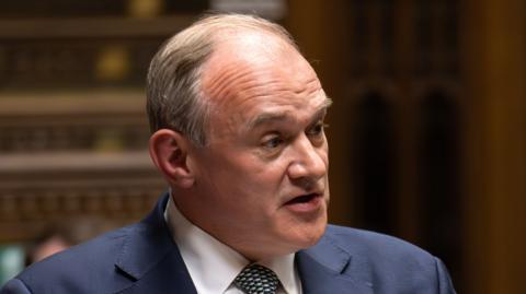 Sir Ed Davey standing up in Parliament. He is wearing a navy suit and tie.