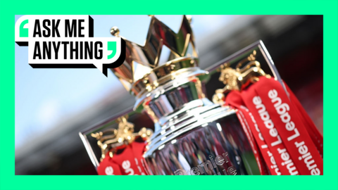 A close-up of the Premier League trophy, adorned with red ribbons, sitting on a plinth on the pitch at Anfield