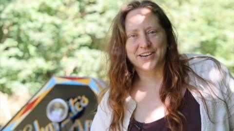 Woman with long brown hear wearing a top and shirt stands in front of a colourful narrowboat