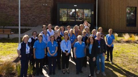 Hospice staff gather outside the Moya Cole building wearing nurses outfits.