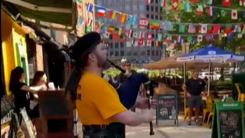 Piper wearing a kilt plays bagpipes outside a pub in Boston
