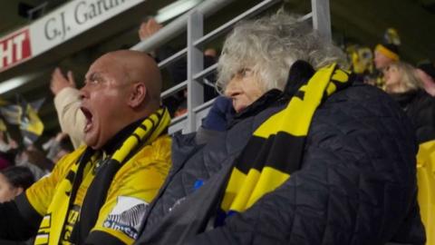 Miriam Margolyes watching the Hurricanes play in Wellington. She wears a black and yellow striped scarf